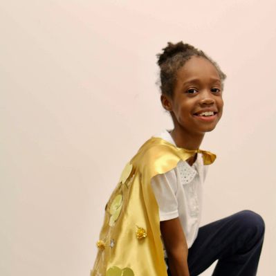 a smiling Black girl in a gold cape crouches