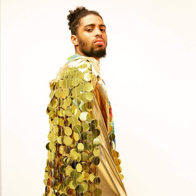 a Black teenager wears a gold cape and looks proud