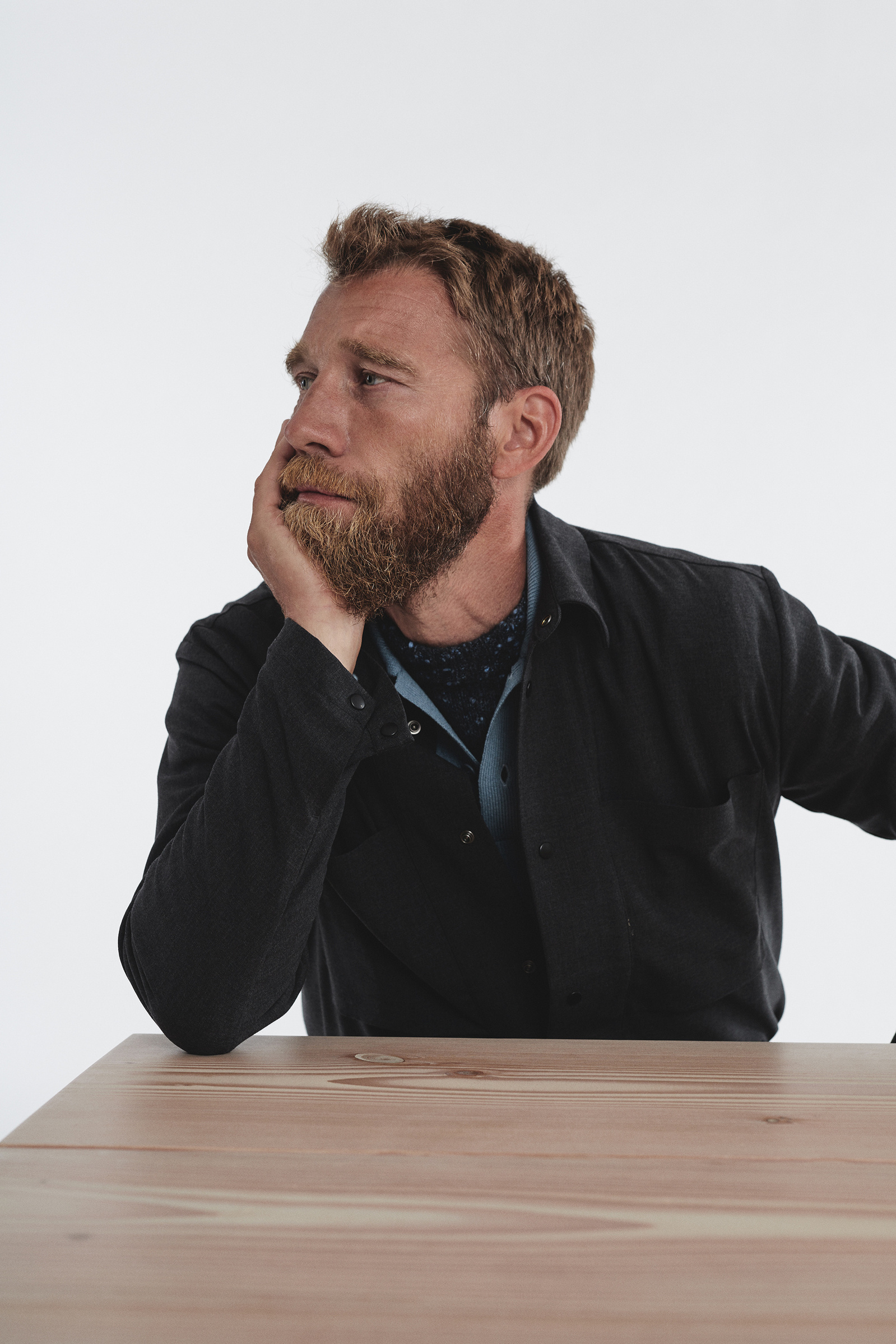 Discover refined style in our captivating fashion image featuring a poised man seated by a rustic wooden table. Dressed in a meticulously crafted shirt paired with a stylish overshirt, this ensemble exudes timeless sophistication.