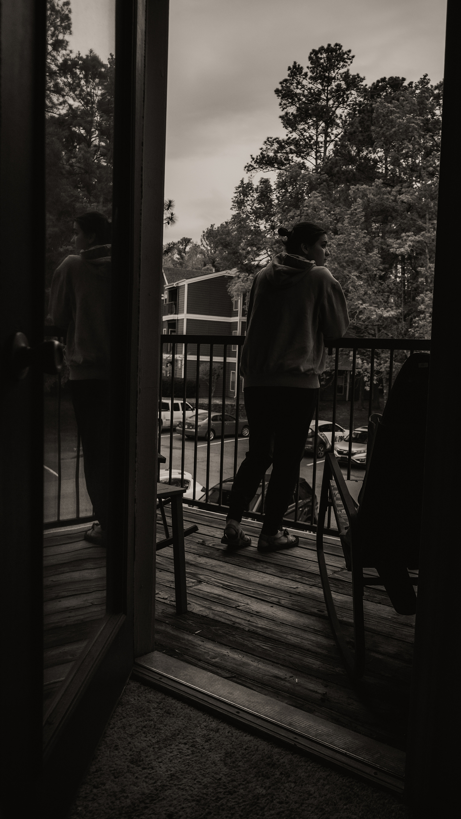 Person standing on a balcony with trees and buildings in the background.