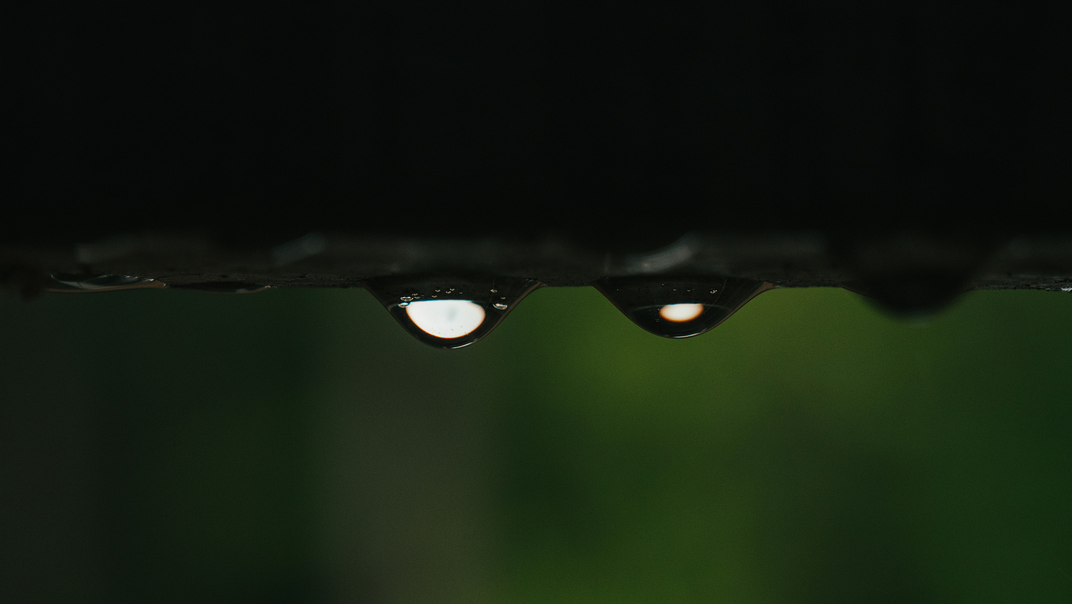 Two raindrops on the bottom of the balcony rail with light reflecting through.