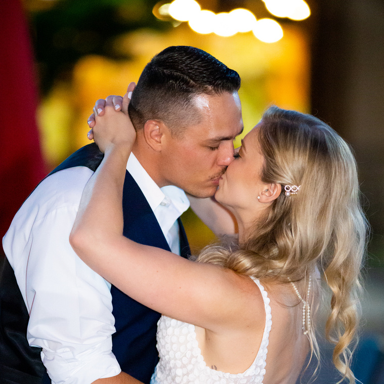 Bride and Groom embracing and sharing a kiss outside of their wedding venue at night time in front of the Holly Vault, in Holly, MI.