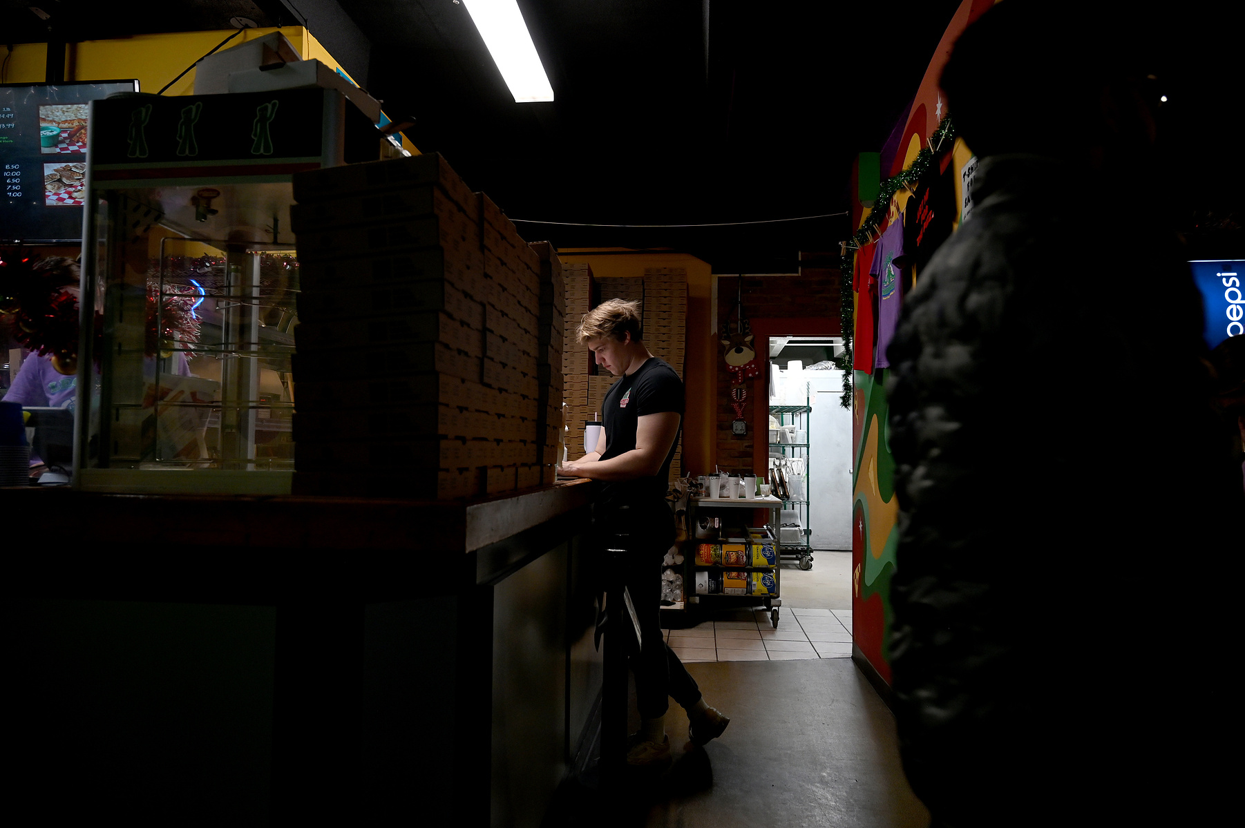 Zack Mikuls, a student at the University of Missouri and a part-time pizza delivery driver, does his homework in the employees only area on Dec. 5, 2024 at Gumby’s Pizza in Columbia. Gen Zers, like Mikuls, are joining the workforce more and more, driven
