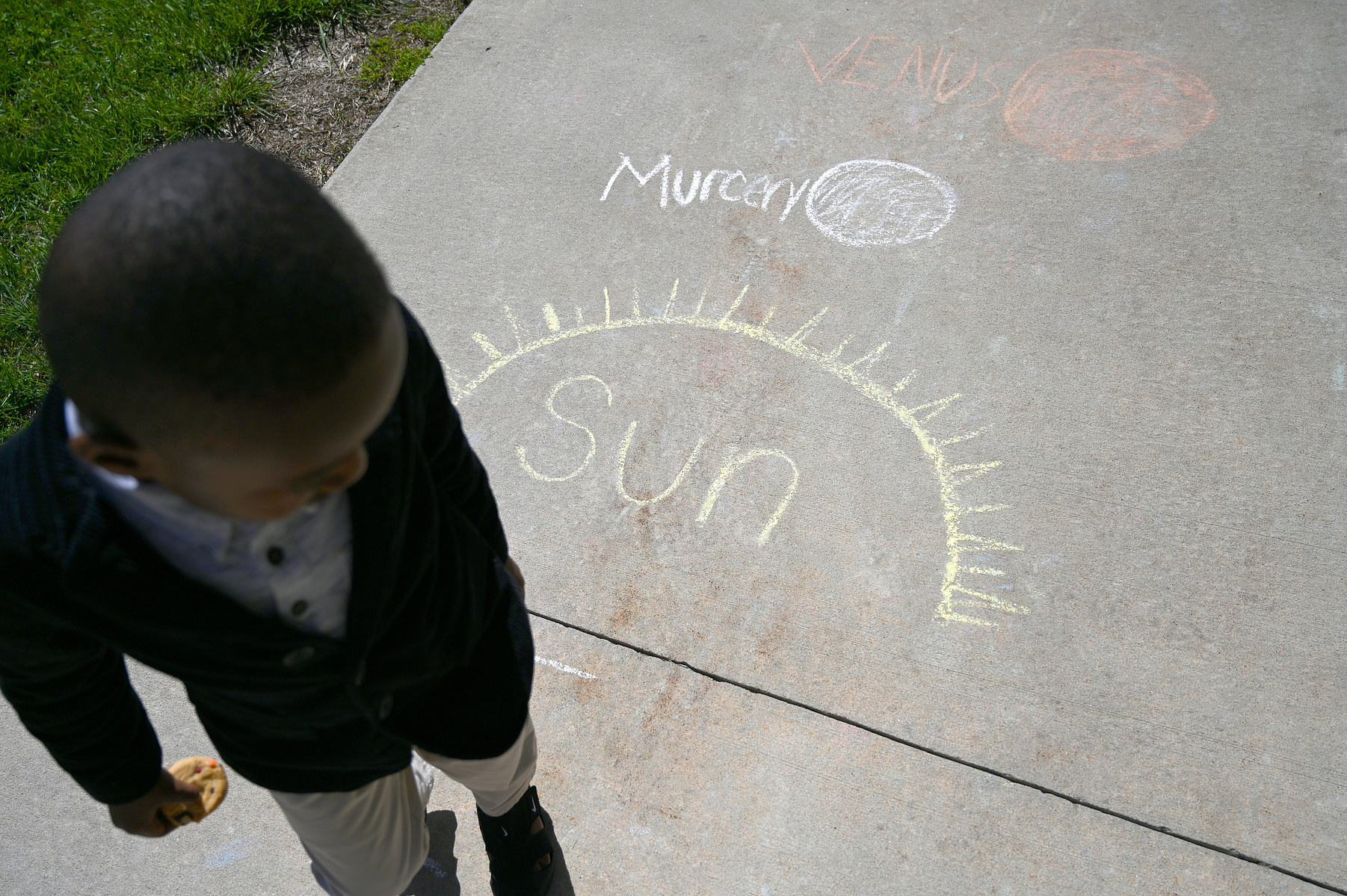 Song Tibuakuu, 5, walks along a chalk drawing of the solar system during the solar eclipse on Monday at the Children’s School at Stephens College in Columbia. “Space travel!” shouted Song as he walked along the path.