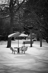 A patio table, chairs and umbrella sit unoccupied in the snow.