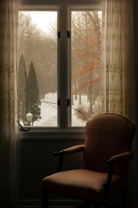Light filters in through a curtained window onto an armchair.
