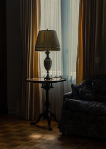 A lamp sits on a round table in a curtained window