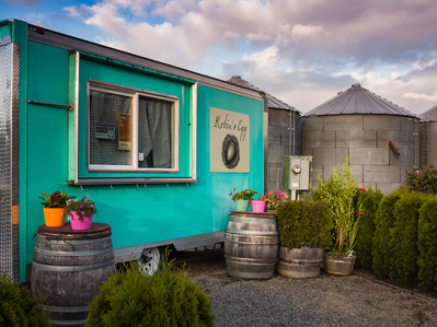 A turquoise trailer home with flower pots sits adjacent to grain silos