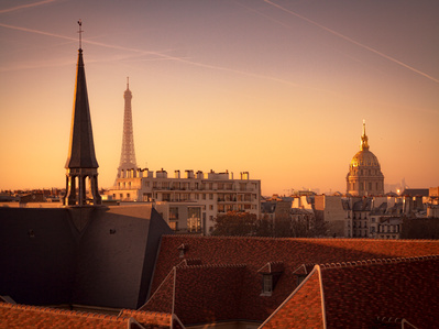 A sunset view of Paris rooftops including the Eiffel Tower and the dome of Les Invalides.