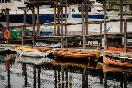 Wooden rowboats tied to a pier and their reflections in the water.