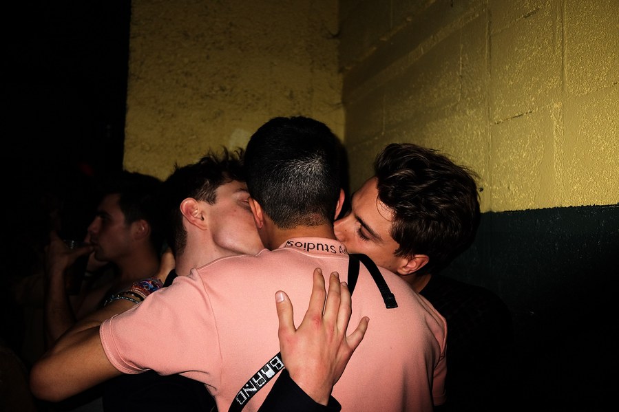 three boys kissing in a club
