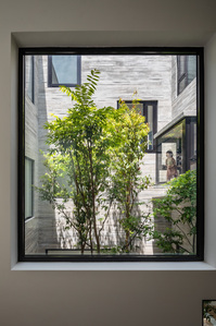 View of the courtyard with a girl at the bay window of the Window House designed by Super Assembly.