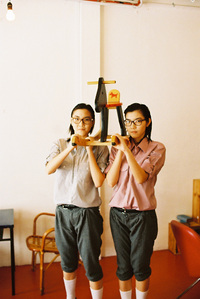 Portrait of a twin holding up a wooden rocking horse in a cafe. The photograph is shot using analog film.