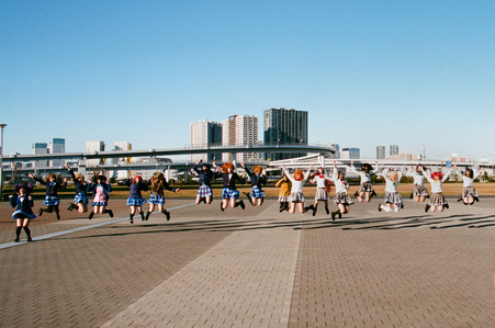 A group of Japanese cosplayers wearing anime school uniforms jumping at the same time. The photo is taken at Odaiba.