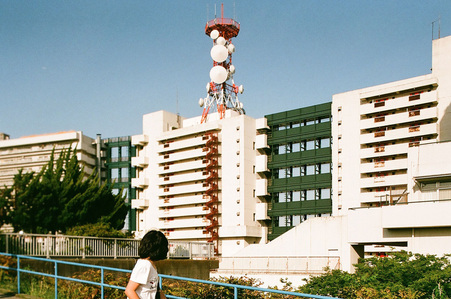 A girl looking at the telecommunication tower on top of a building block in Tokyo.