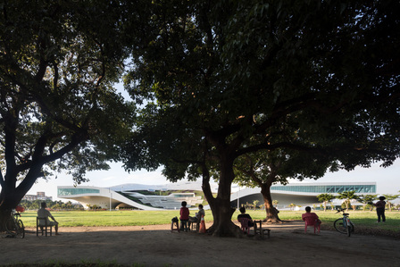 Elderly people sitting under the trees looking at National Kaohsiung Center for the Arts in Taiwan, designed by Mecanoo architecten.