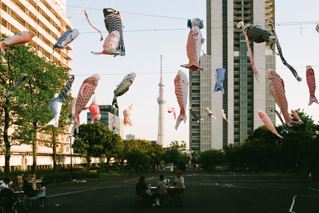 A group of Japanese people sitting under Koinobori with Tokyo Skytree in the background.