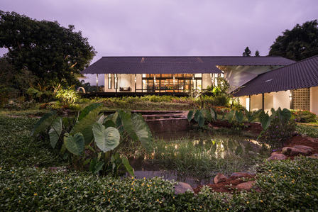 Evening view of Sukasantai Farmstay in Indonesia designed by Goy Architects, with a pond in the foreground.
