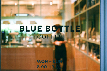 View through the shopfront glass of a Blue Bottle Coffee outlet in Japan with staff in the background.
