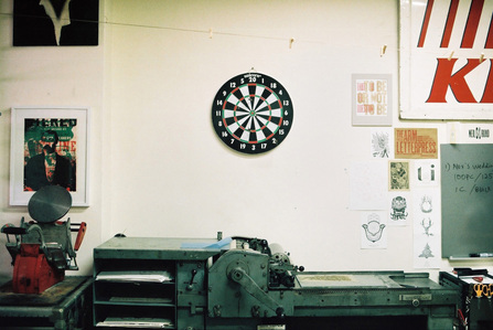 Dartboard hanging on the wall above a letterpress machine at the Gentlemen's Press studio by Michelle Yu