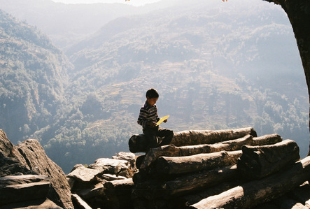 A Nepalese boy sitting on top of tree logs reading a letter in the Annapurna region in Nepal.