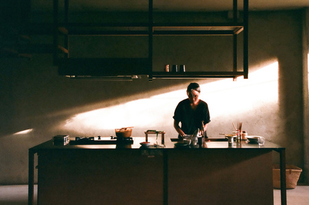 A lady cooking at the kitchen at the House at Carlton Ave designed by Linghao Architects.