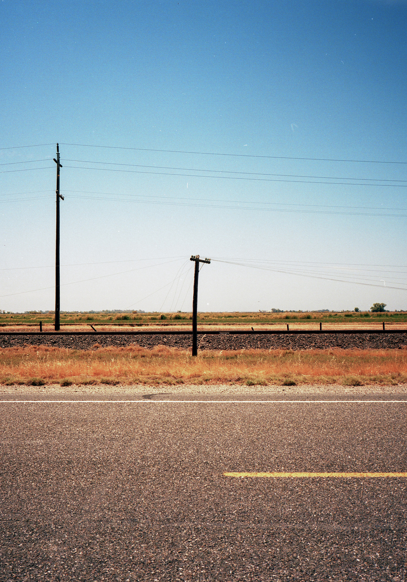Telephone poles and wires, with highway in the foreground. Central Valley of California. Shot on Fuji GA-645i medium format film camera