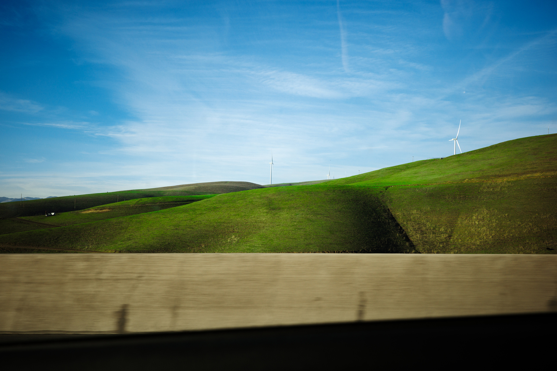 Serene Landscape with Rolling Green Hills and Wind Turbines
This picturesque photograph captures the essence of sustainable energy and natural beauty. Rolling green hills stretch across the frame under a vibrant blue sky, with wind turbines standing as s