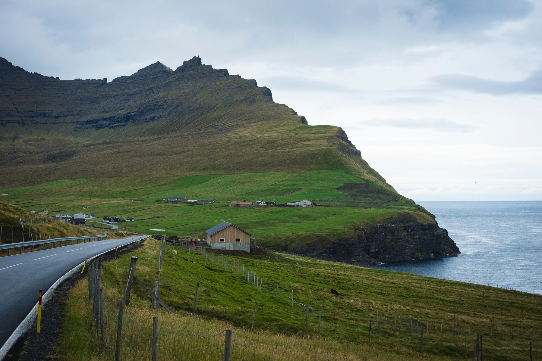 Shot on Fuji XT-2, this breathtaking landscape captures the winding coastal road leading to Viðareiði, the northernmost settlement in the Faroe Islands. The image showcases the dramatic Malinsfjall mountain rising majestically above the village, with