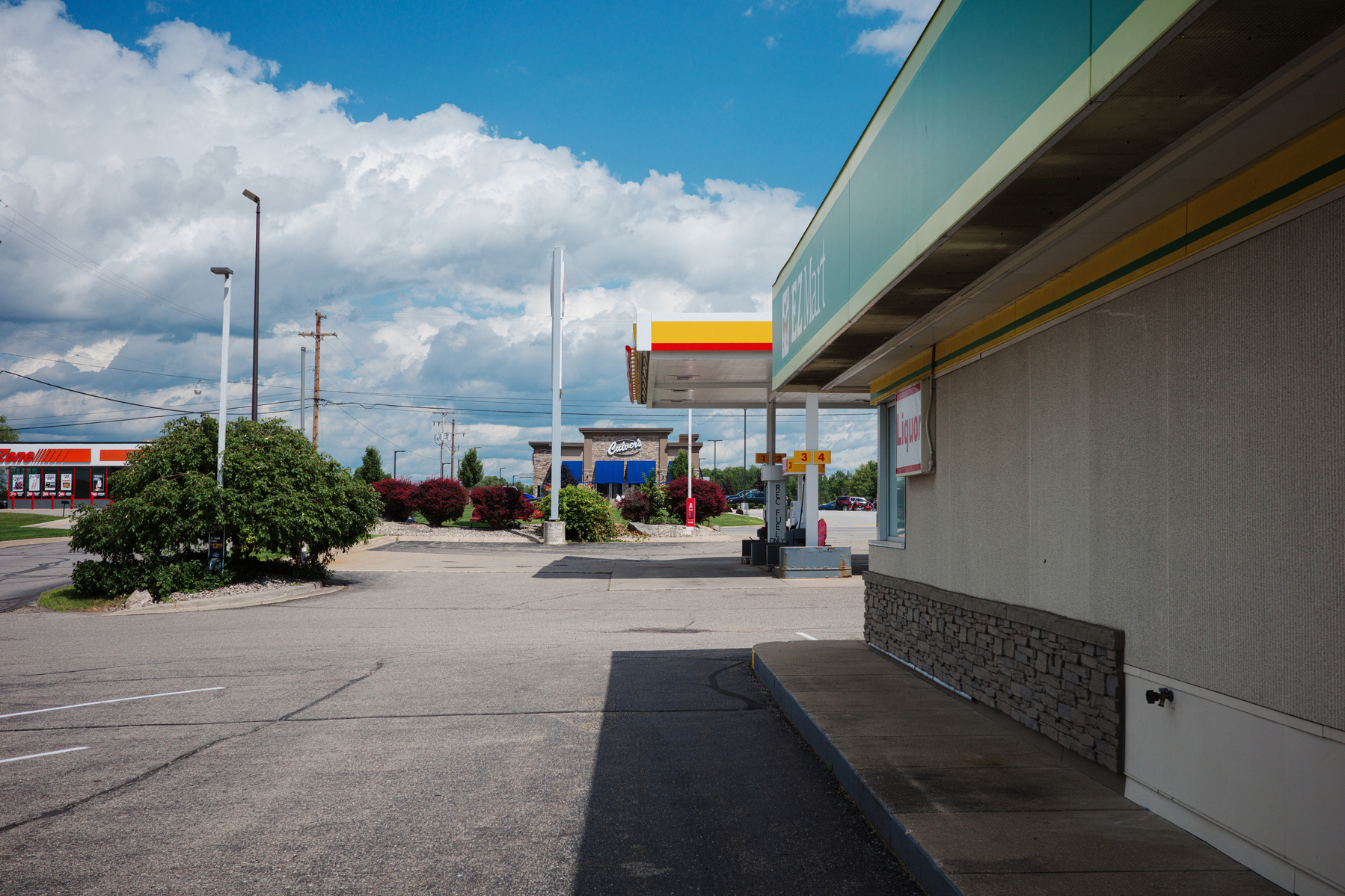 Experience the charm of small-town America with this vibrant photo of a gas station in Clare, Michigan, captured on a Ricoh GR camera. The image features a serene suburban scene with a gas station, clean architecture, and lush landscaping under a bright b