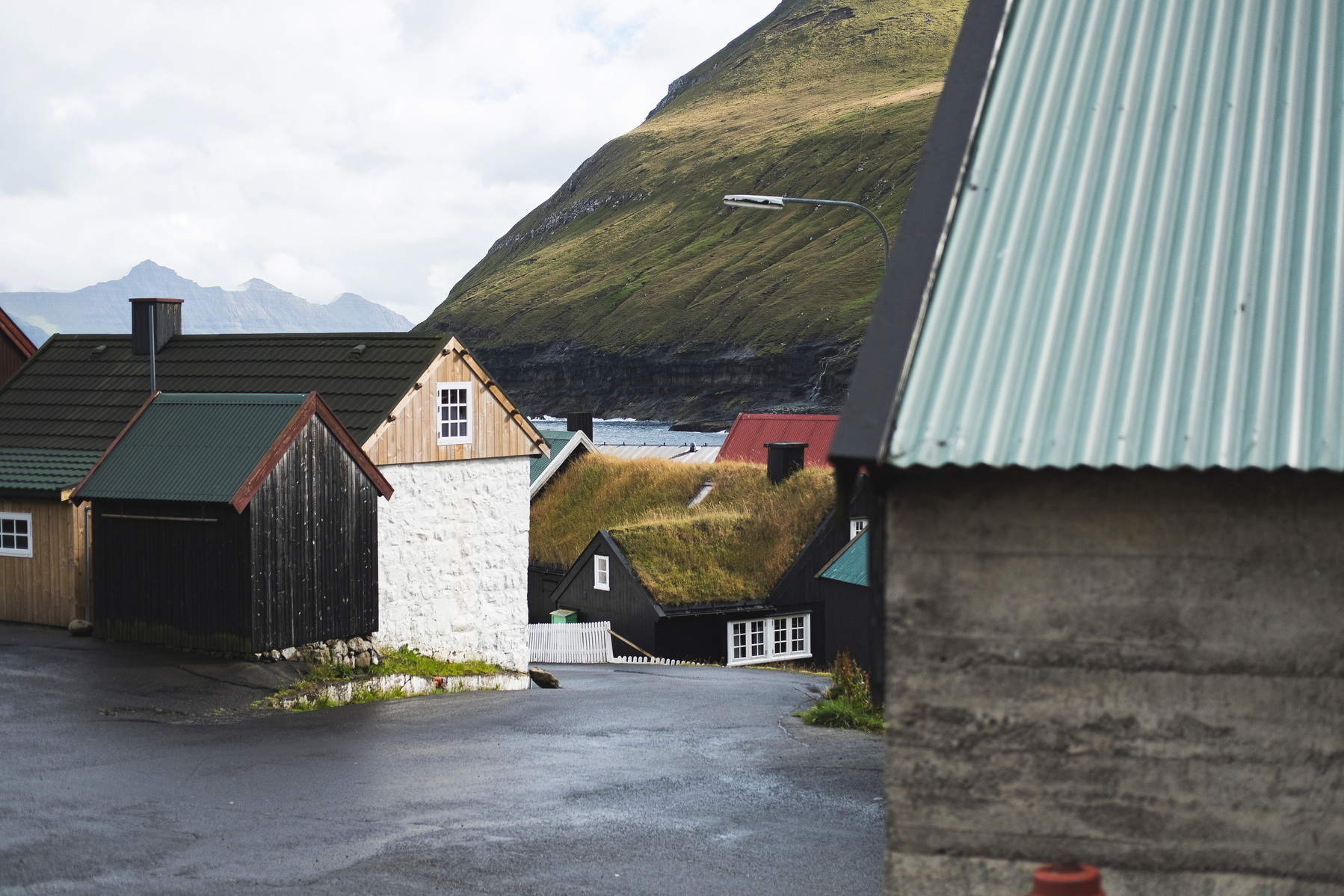 Captured on Fuji XT-2, this atmospheric photograph showcases the authentic charm of Gjógv, a remote village in the Faroe Islands. The image features distinctive Nordic architecture, including traditional houses with grass-covered roofs and a mix of wood