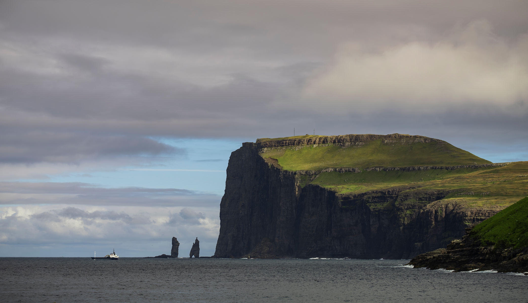 Captured on a Fuji XT-2, this dramatic seascape showcases the legendary Risin og Kellingin (The Giant and The Witch) sea stacks against the towering 343-meter Eiðiskollur cliffs on Eysturoy, Faroe Islands. The moody atmosphere is enhanced by breaks of blu