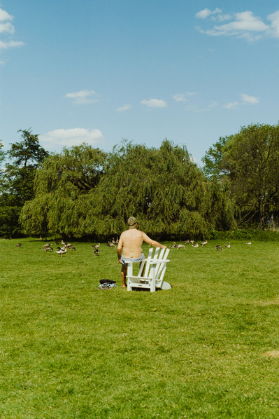 Elderly half naked man sitting on a chair in front of a flock of geese. Shot on Canon F1, Portra 400.