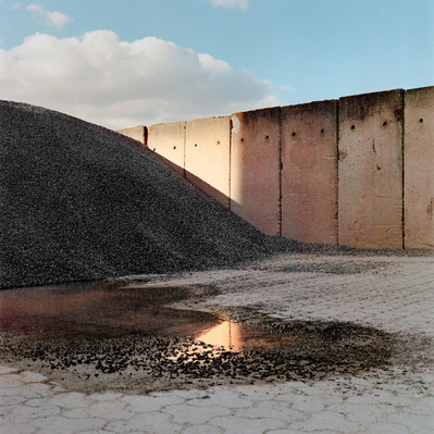 A pile of gravel, a concrete wall and a puddle in the foreground reflecting golden sunlight. Shot on Hasselblad 500CM, Portra 400.
