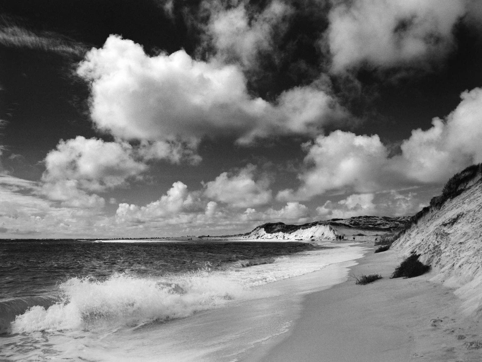 Dramatic black and white photo of waves crashing on a beach with dunes. Hasselblad 500CM using a red filter, Kodak Gold 200.