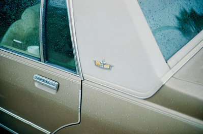 Moody photo of a vintage Chevrolet in the rain, teal and orange color grading. Shot on Canon F1, Portra 400.