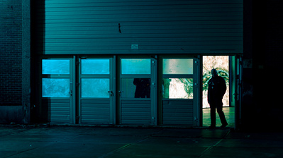 Cinematic scene of an industrial building with a man walking out the door at night.