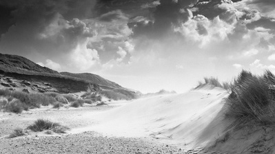 Black and white photo of sand dunes and clouds in the sky.