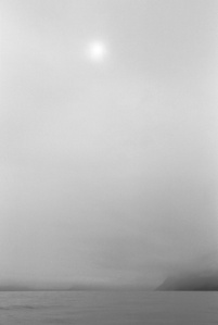 The sun shines through clouds over the sea at a fjord