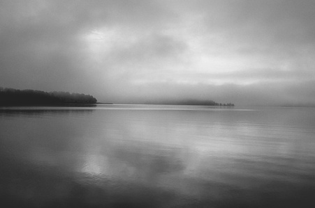 Calm water surface on a foggy bay with appearing peninsulas on another side