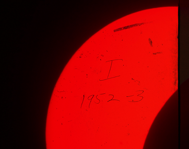 A moody photo-collage depicting a partial solar eclipse. The sun is bright red and crescent-shaped against a black background as the earth's shadow recedes across its face.