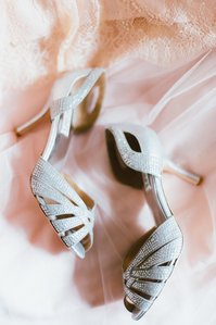 Silver bridal shoes laying on top of a blush bridesmaid gown.