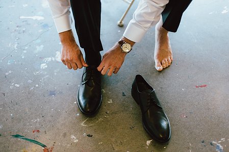 The groom ties his shoes on the work floor of Artitst for Humanity in Boston