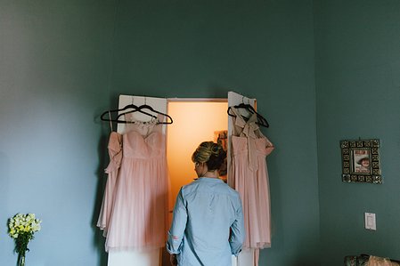 A bridesmaid walks through blush bridesmaid gowns during wedding preparations.