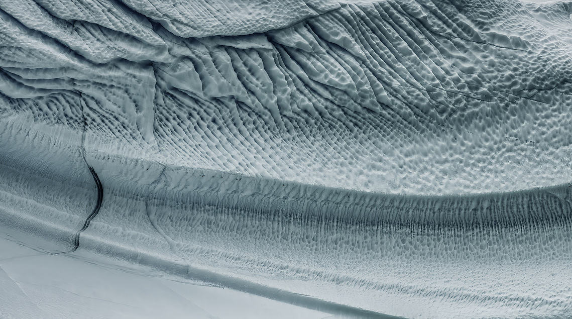 Close-up view of layered glacier ice marked by rippled textures, compressed folds and a dark fracture line.