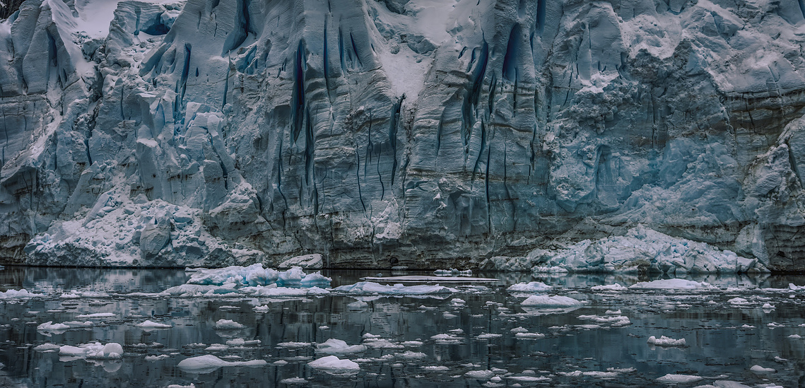 A monumental blue glacier front rising above dark water scattered with fragments of sea ice.