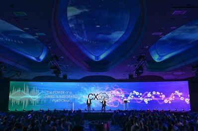 two corporate company executives presenting at the company's annual summit in front of hundreds of company employees. Huge projection display behind them