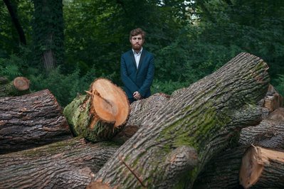 portrait of musician Sagi Shachar known as James Dawn in Prospect Park wearing a suit surrounded by trunks