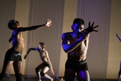 three shirtless contemporary dancers dancing under white an blue light