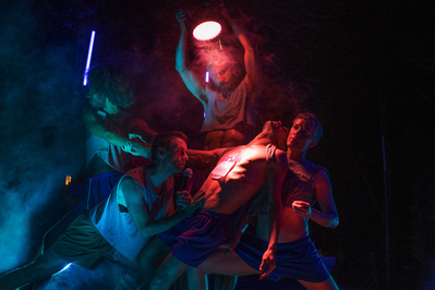a group of gay male dancers dancing in colored lighting among smoke